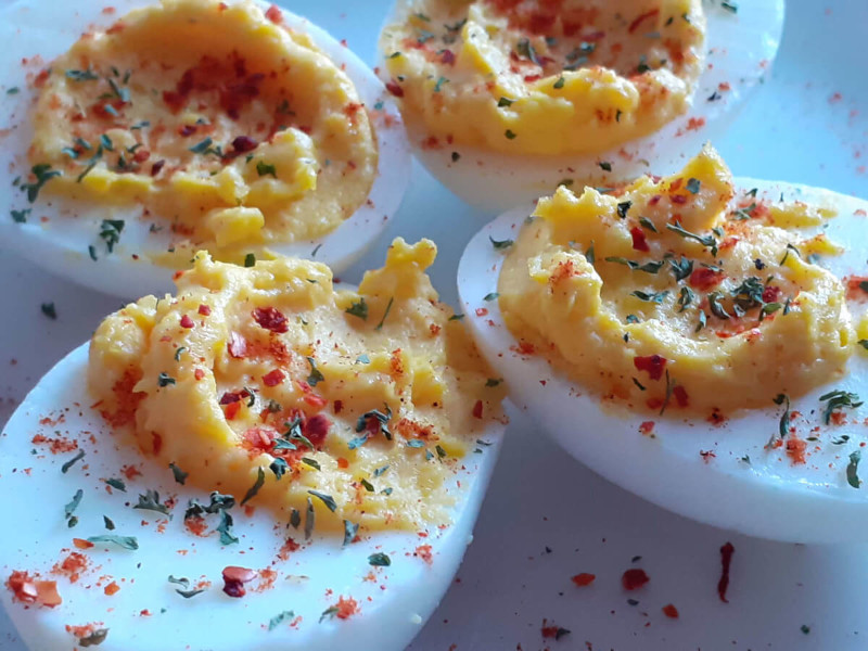 Four deviled eggs on a white plate garnished with Parsley, Aleppo and Paprika.